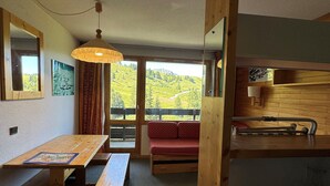 A cozy room with a wooden table, benches, a red cushioned bench, a hanging light fixture, and a view of green hills through large windows. - Apartment with balcony and direct slope access, pets allowed (Belle Plagne)