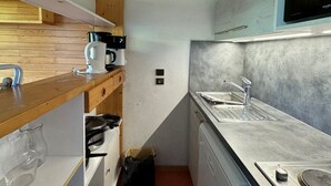 A compact kitchen with wooden cabinets, a built-in stove, a coffee maker, and a microwave. - Apartment with balcony and direct slope access, pets allowed (Belle Plagne)