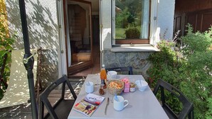 An outdoor dining area with a table set for two, a magazine, and a basket of bread. - Comfortable semi-detached chalet 8 pers · Shuttle to slopes · Free WIFI · Terrace (La Salle-les-Alpes)