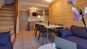 A modern kitchen with a microwave, stove, and sink. There is a dining area with a table and chairs, and a sofa with a laptop on it. - Comfortable semi-detached chalet 8 pers · Shuttle to slopes · Free WIFI · Terrace (La Salle-les-Alpes)