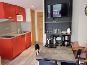 A compact kitchen with red cabinets, a microwave, a sink, and a dining area with chairs and a table. - Renovated studio 3 pers, near slopes, wellness (La Plagne Montchavin Les Coches)
