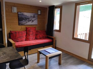 A cozy room with a wooden wall, a sofa with red cushions, a small table, and a chair.