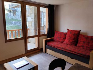 A room with a wooden sofa, a small table, and a window with a view of a stone building.