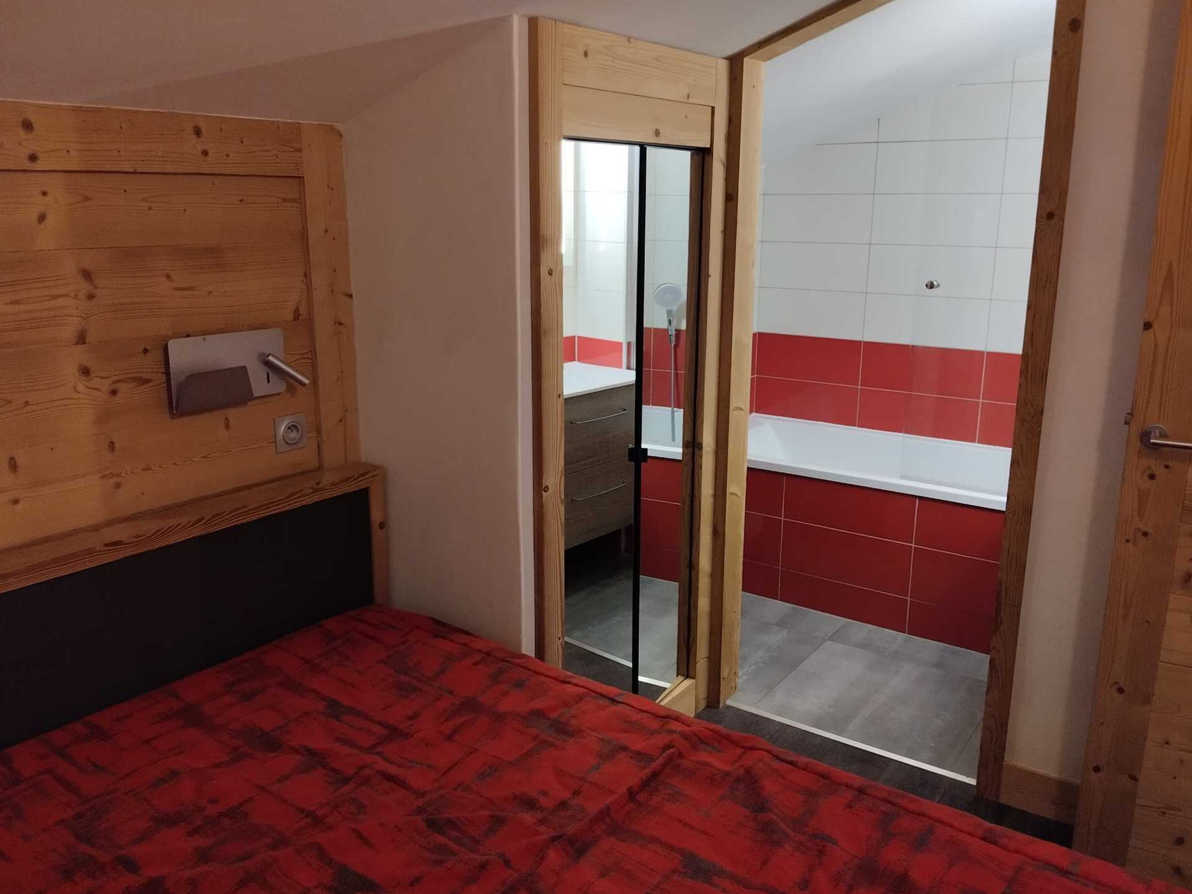 A room with a bed, a wooden headboard, a sliding door leading to a bathroom, and a red and white tiled wall.
