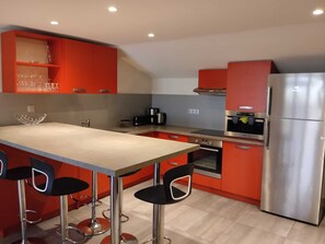 Une cuisine moderne avec des meubles de rangement rouges, des appareils électroménagers en acier inoxydable, un îlot central doté de tabourets et un four encastré.