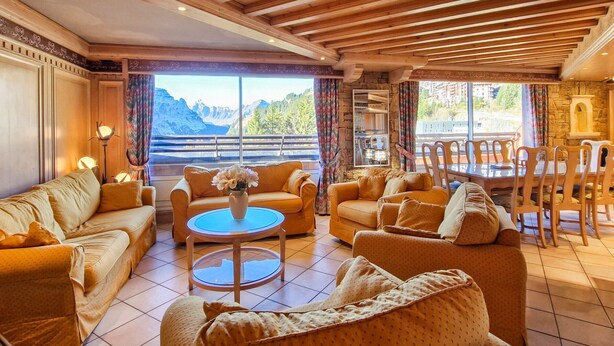 A cozy living room with wooden beams, a fireplace, and a scenic mountain view.