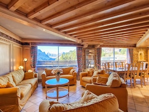 A cozy living room with wooden beams, a fireplace, and a scenic mountain view.
