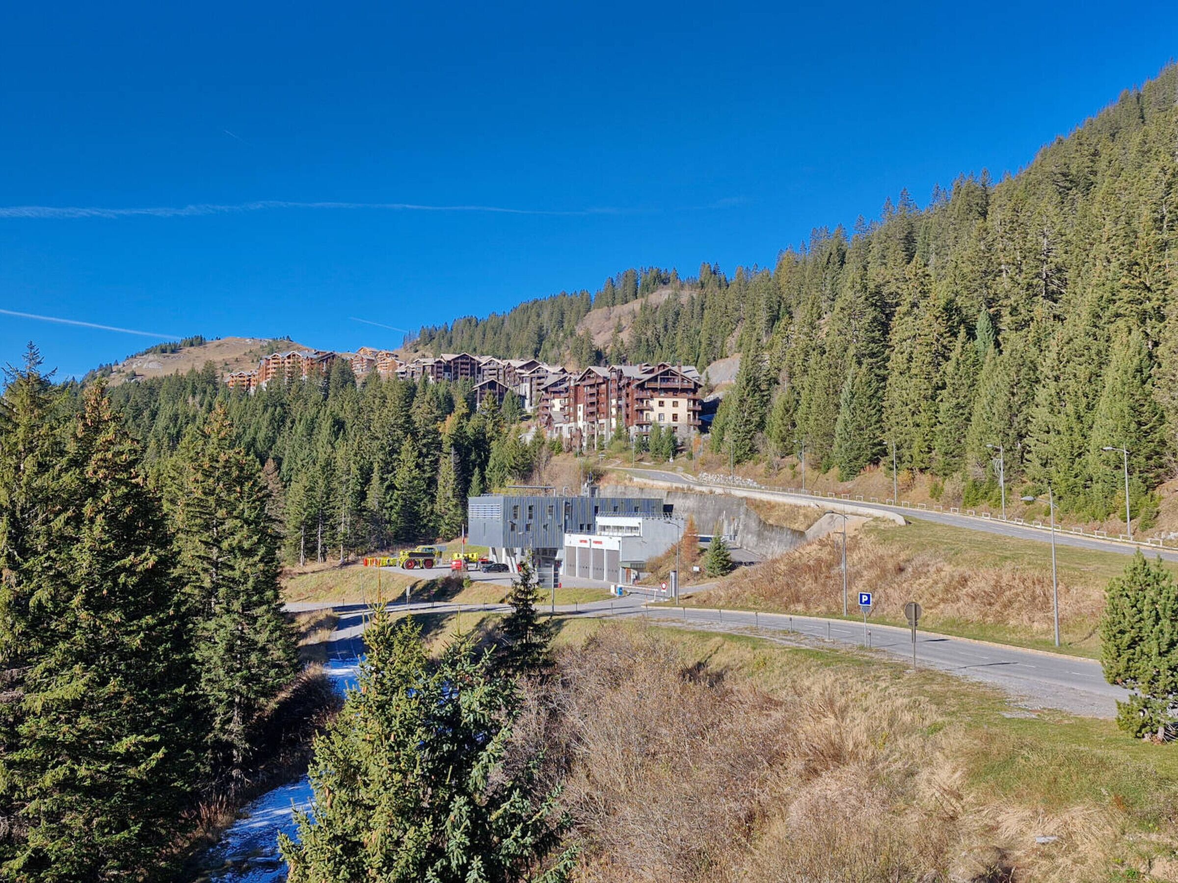 A mountain resort with a ski lift, a parking area, and a road leading to a building complex.