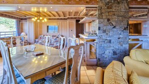 A wooden dining area with a glass table, white chairs, and a stone fireplace.