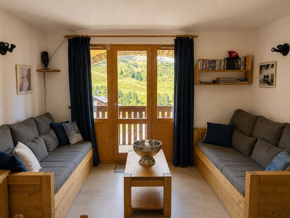 Une pièce chaleureuse avec deux canapés, une table en bois et une vue sur un paysage montagneux, visible à travers une grande porte.