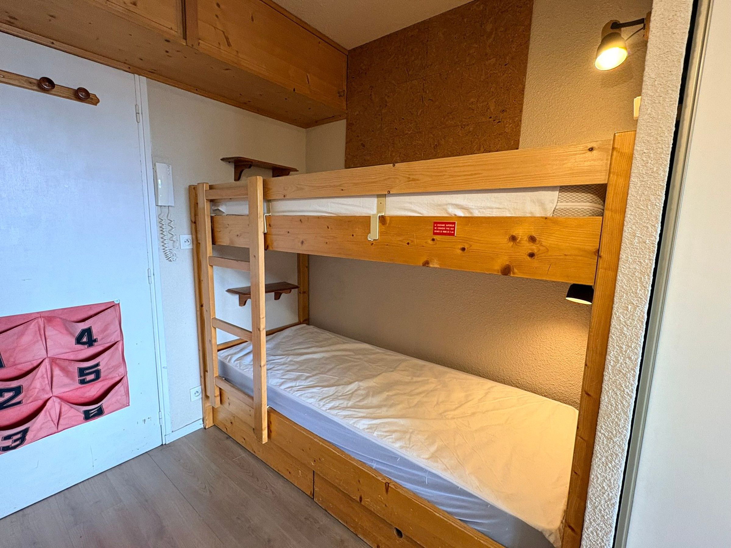 A bunk bed with a ladder, a small shelf, and a red sign with numbers.