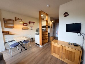 A compact living space with a dining area, kitchenette, and a television mounted on the wall.