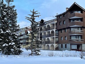 A multi-story hotel with balconies, snow-covered surroundings, and a mountainous backdrop.