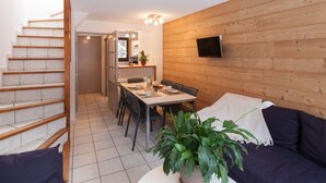 A compact living space with a dining area, a sofa, a staircase, and a TV mounted on the wall. - Bright triplex chalet, shuttle to slopes, Wifi, pets allowed (La Salle-les-Alpes)