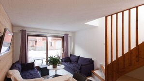A cozy living area with a sofa, dining table, and a staircase. - Bright triplex chalet, shuttle to slopes, Wifi, pets allowed (La Salle-les-Alpes)