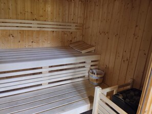 Un cuarto de sauna con bancos de madera, un cubo y un banco con cojín negro.