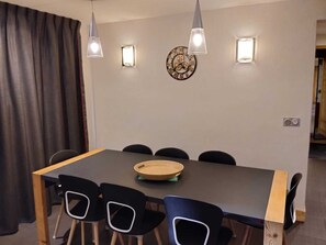 Un comedor con una mesa, sillas, lámparas colgantes y un reloj de pared.