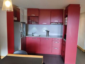 Eine kleine Küche mit rosa Schränken, einer Edelstahl-Spüle und einem Kühlschrank.