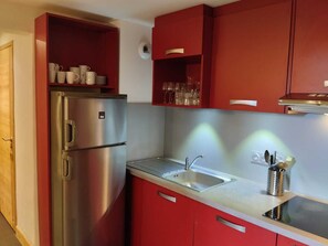 Cocina compacta con refrigerador de acero inoxidable, un lavamanos y armarios color rojo.