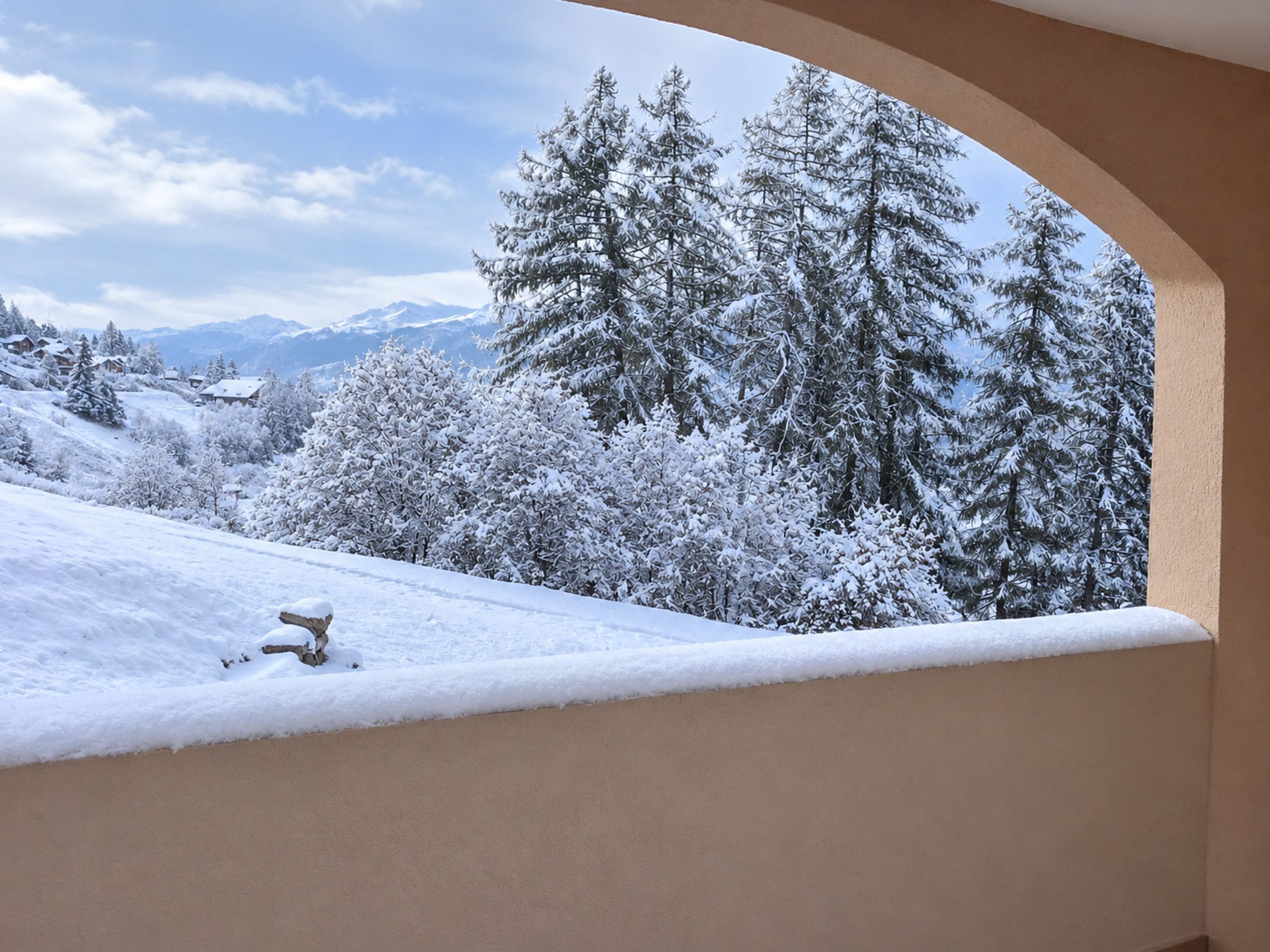 Un paysage enneigé, avec des arbres et des montagnes en arrière-plan, vu à travers une fenêtre incurvée.