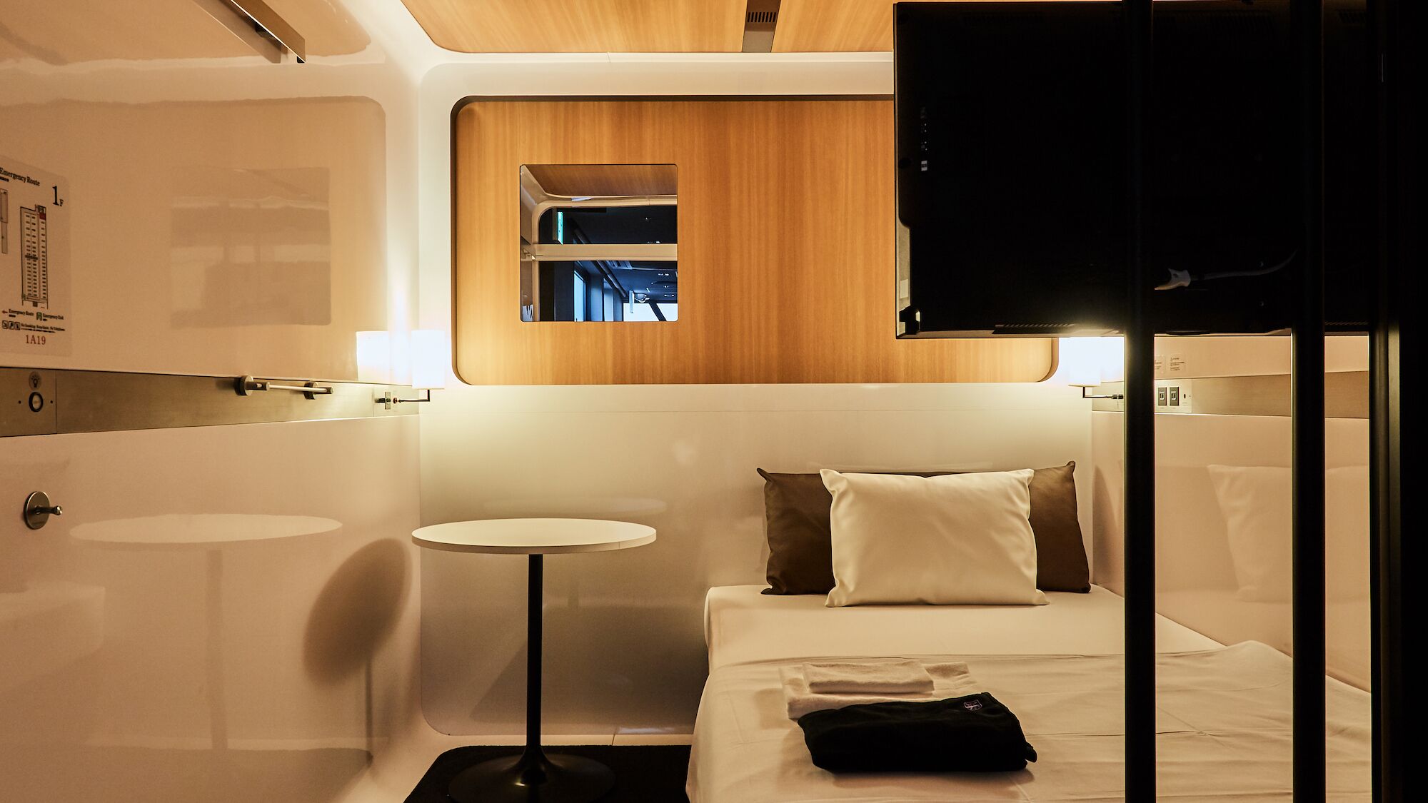 A compact, modern hotel room with a bed, bedside table, and a small round table.