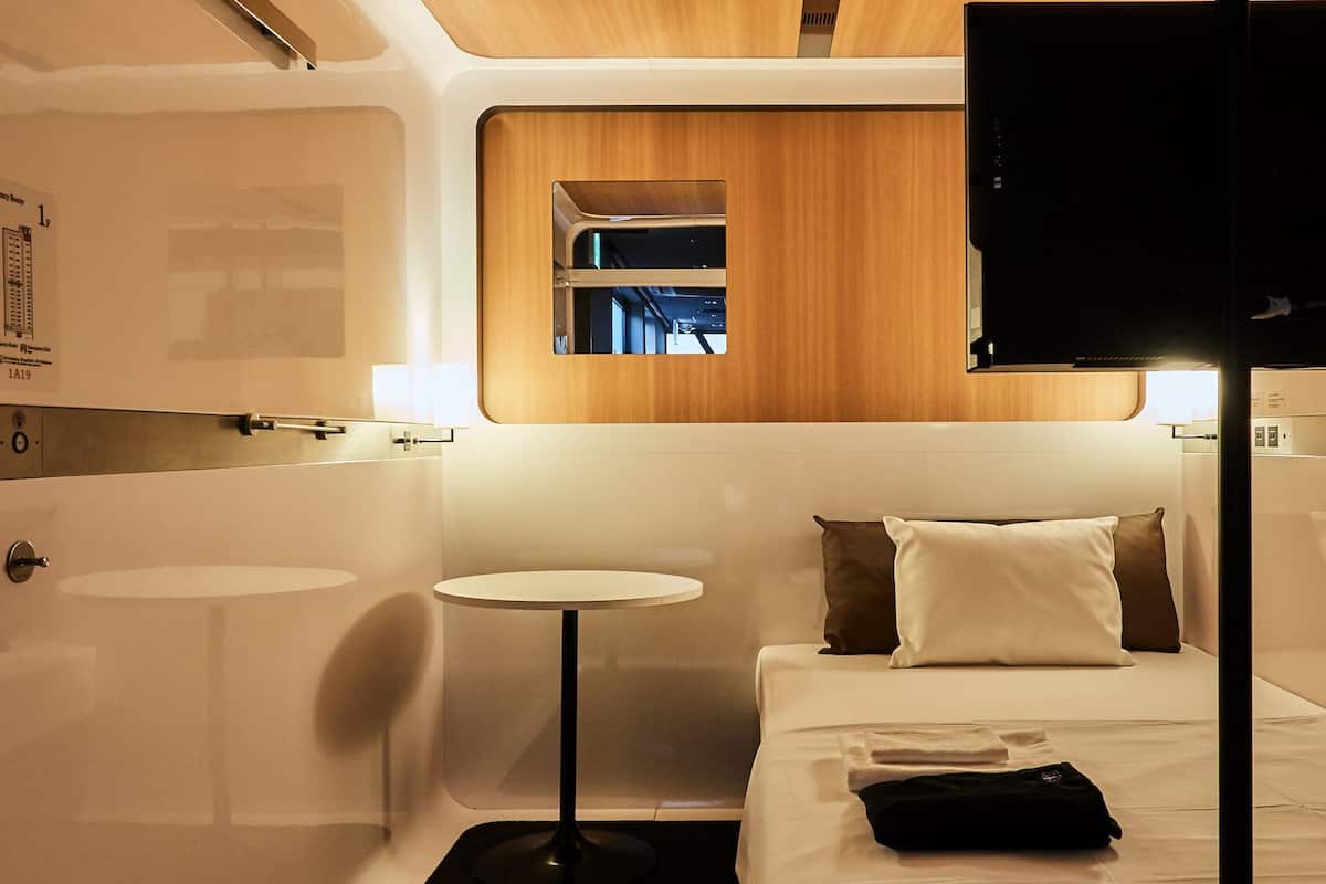 Une chambre d’hôtel moderne et compacte, comprenant un lit, une table de chevet et une petite table ronde.