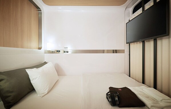 A compact, modern room with a bed, a flat-screen TV mounted on the wall, and a small control panel above the bed. - First Cabin Nishi Umeda (Osaka)