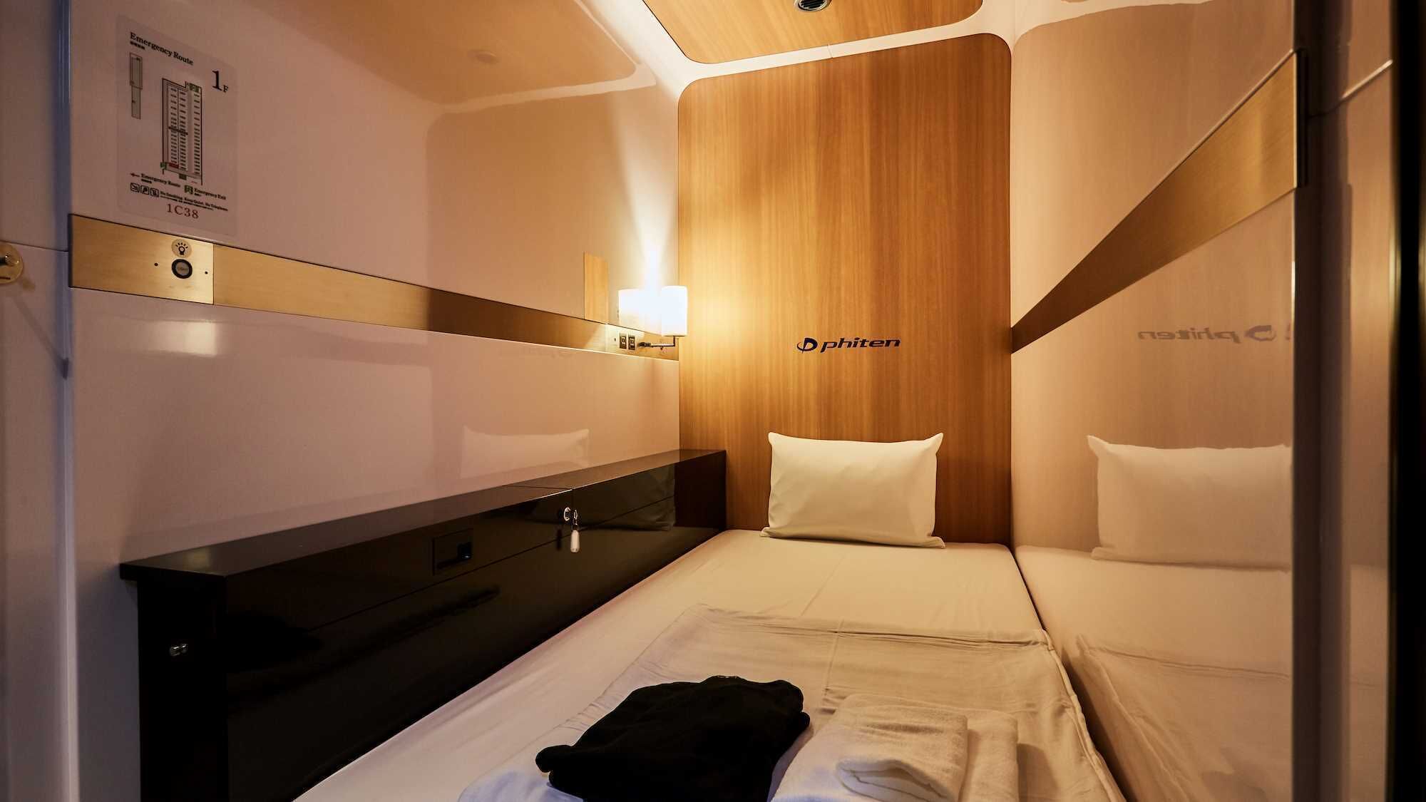 A compact hotel room with a wooden accent wall, a bedside table, a mirror, and a bed with pillows.