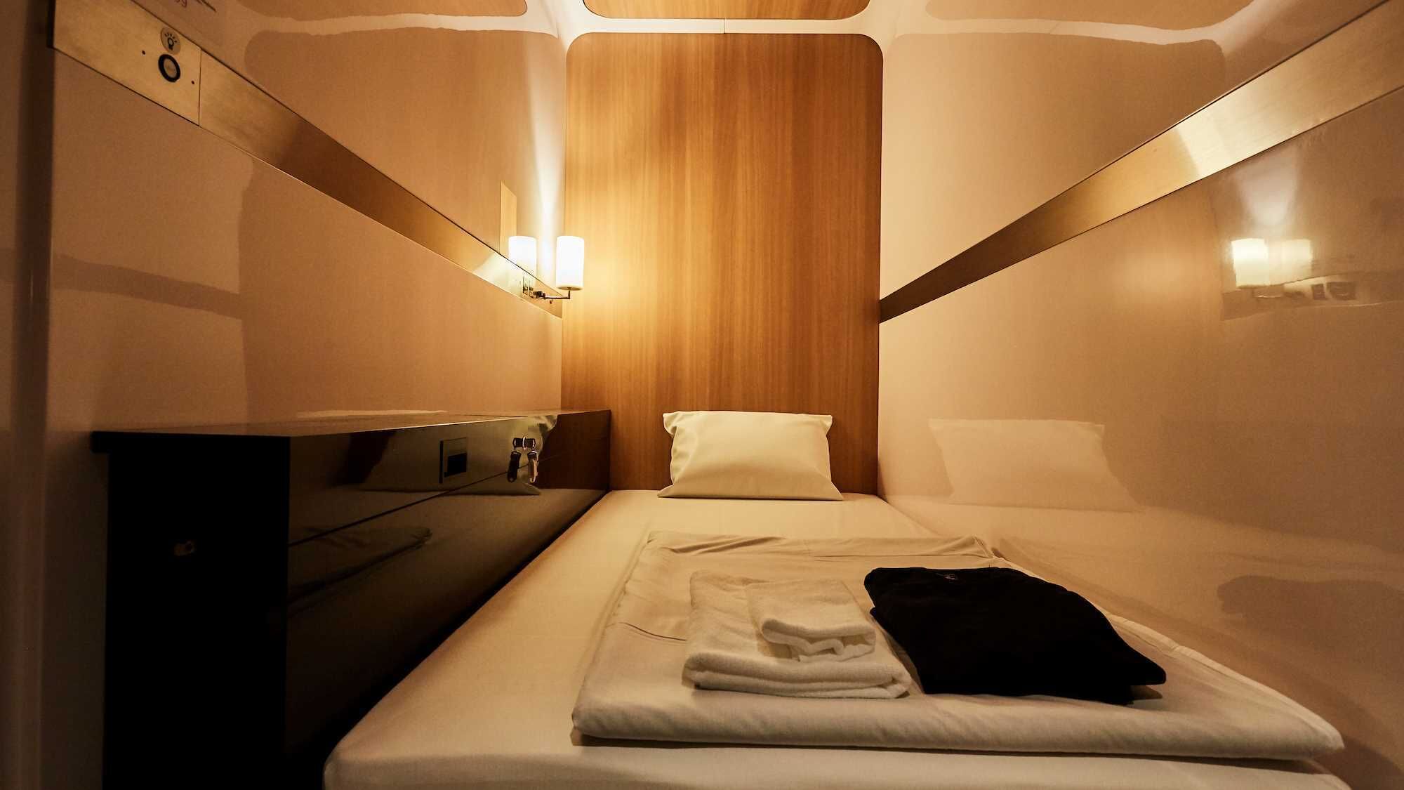 A compact hotel room with a bed, bedside table, lamp, and a wooden panel wall.