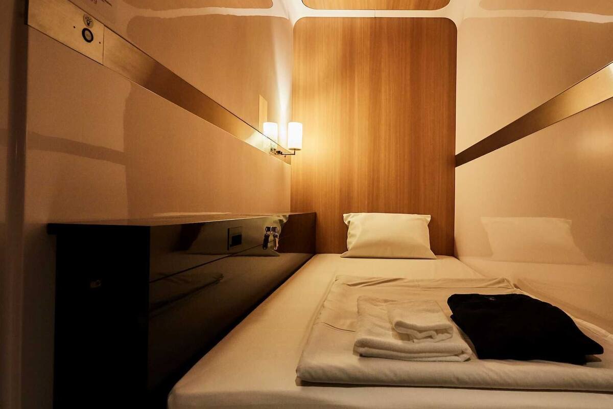 Une chambre d’hôtel de taille réduite, comprenant un lit, une table de chevet, une lampe et un mur recouvert de panneaux en bois.