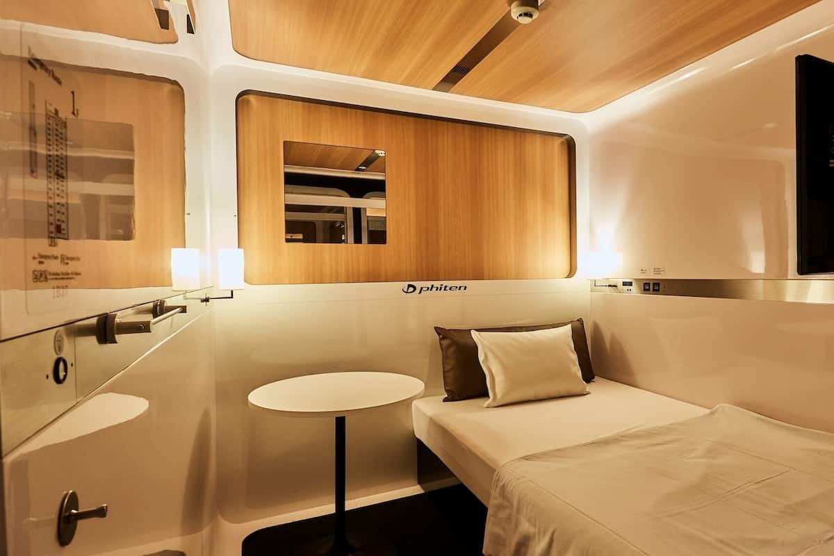 Un compartiment de train moderne avec un plafond en bois, une petite table ronde, un lit avec des oreillers et un miroir.