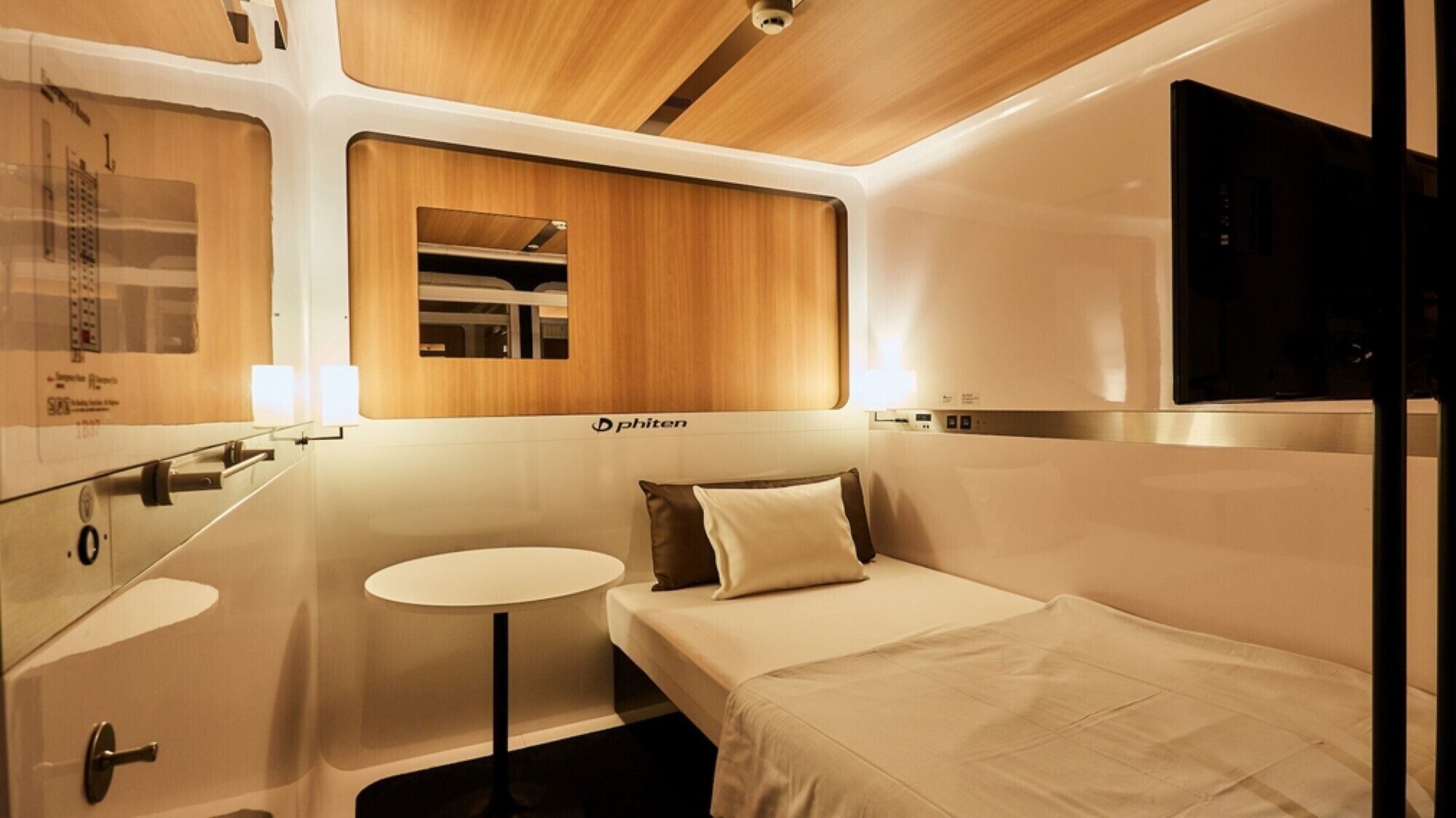 A compact, modern train cabin with a bed, a small table, and a mirror.