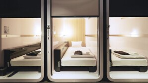 A hotel room with three beds arranged in a row, each with a bedside table and lamp. - First Cabin Nishi Umeda (Osaka)
