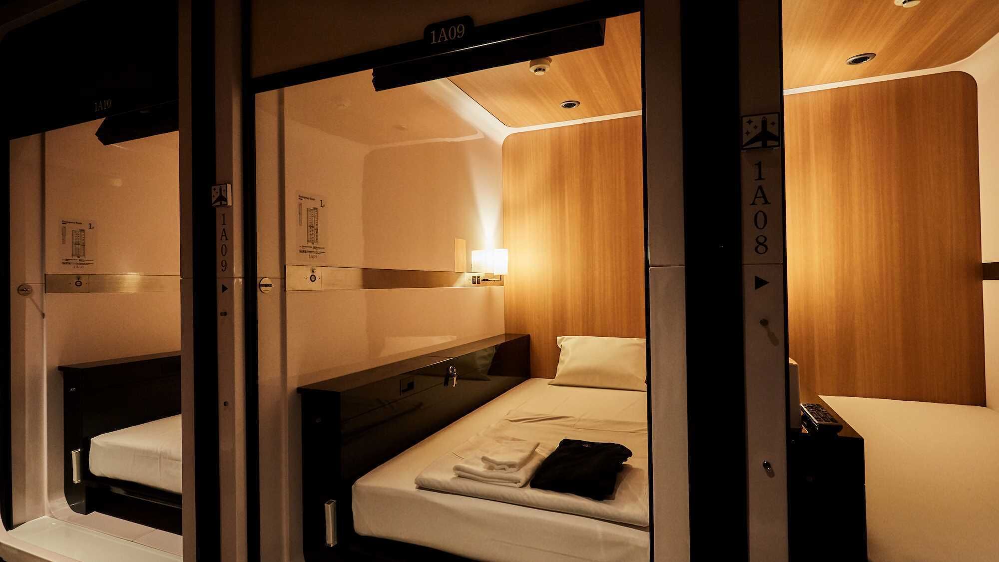 A hotel room with a bunk bed, a bedside table, a lamp, and a small desk with a chair.