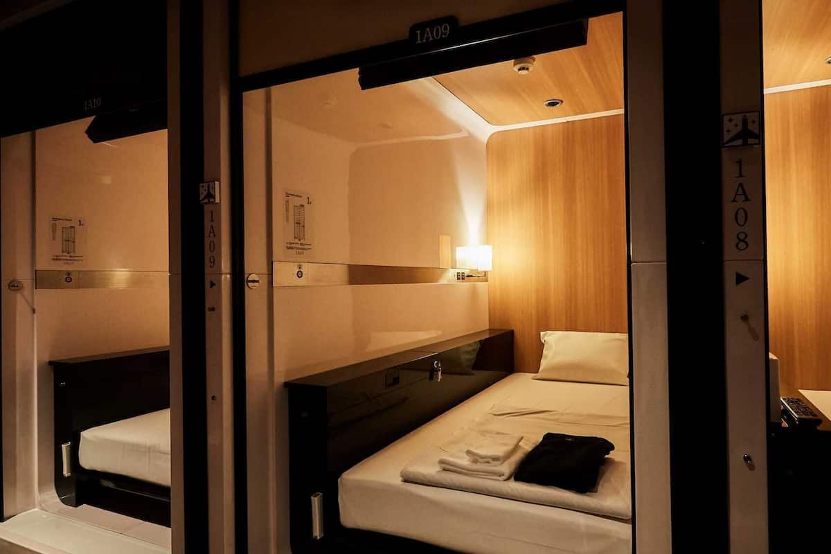 Une chambre d’hôtel avec un lit superposé, une table de chevet, une lampe et un petit bureau avec une chaise.
