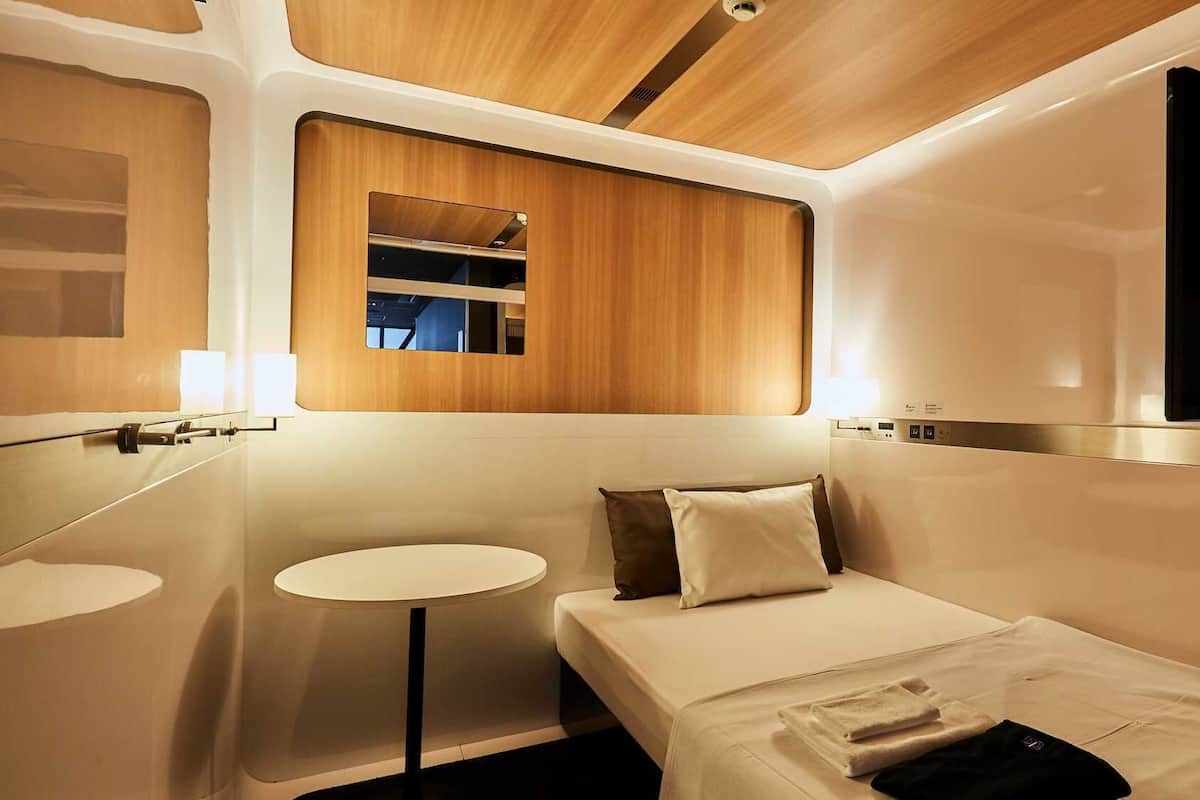 Une chambre d’hôtel moderne et compacte, comprenant un lit, une table de chevet, un miroir et une petite table ronde.