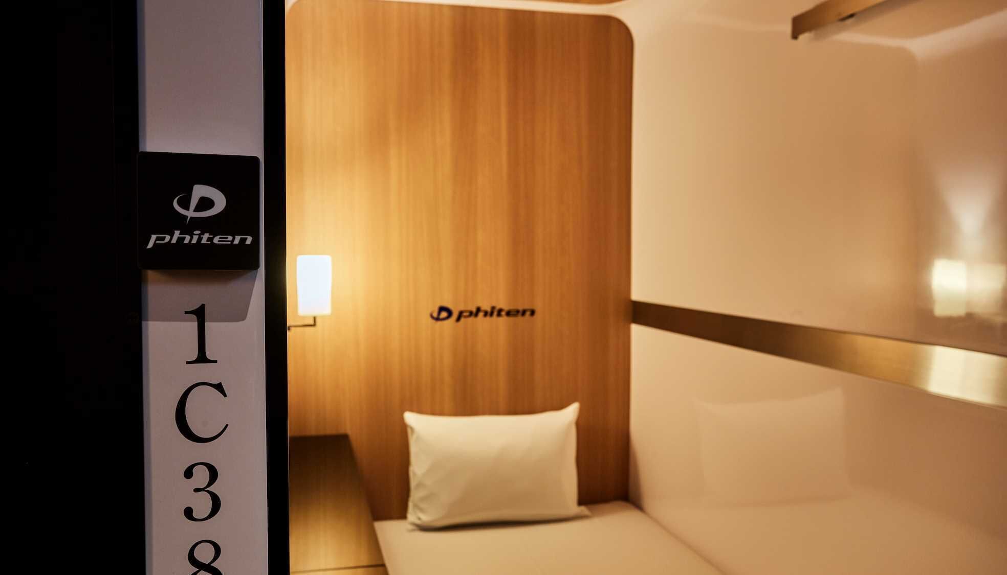 A hotel room with a wooden headboard, a white pillow, and a sign with the 'phiten' logo.