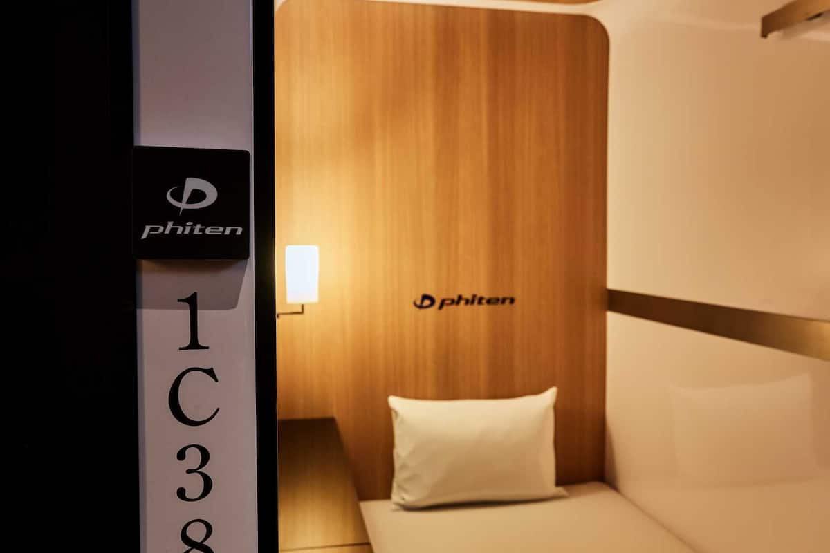 Une chambre d’hôtel avec une tête de lit en bois, un oreiller blanc et une enseigne portant le logo « Phiten ».