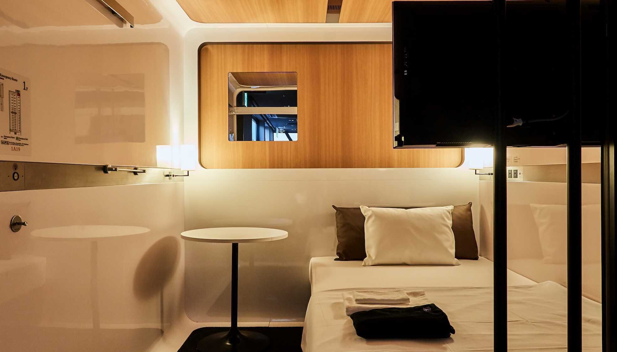 A compact hotel room with a bed, a small round table, a mirror, and a TV.