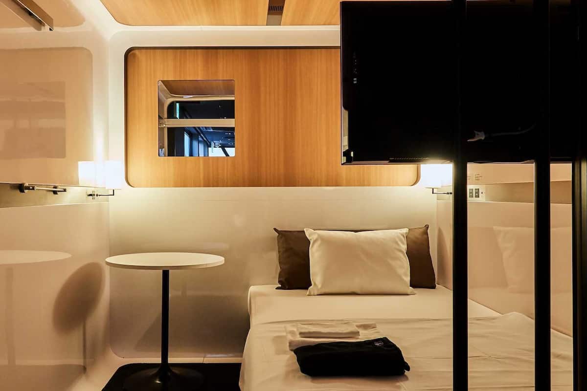 Une chambre d’hôtel de taille réduite, comprenant un lit, une petite table ronde, un miroir et un téléviseur.