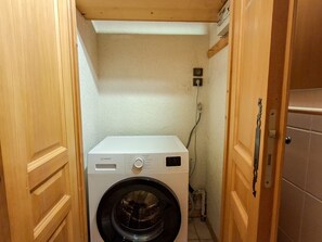 Ein kleiner Hauswirtschaftsraum mit einer Waschmaschine mit Frontlader, Holzschränken und Fliesenboden.