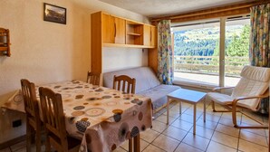 Ein gemütliches Zimmer mit Esstisch, Stühlen, einer Couch und einem Fenster mit Blick auf einen Wald.