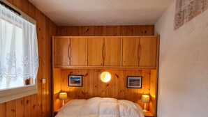 Ein Schlafzimmer mit Holzwandverkleidung, einem Bett mit Bettdecke, zwei Nachttischlampen und zwei gerahmten Bildern an der Wand.