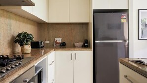 Una cucina moderna con mobili bianchi, un frigorifero in acciaio inossidabile, un piano cottura a gas e un bancone con una pianta e un cesto.