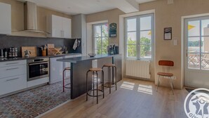 Een moderne keuken met een centraal eiland, een paar barstoelen en uitzicht op de buiten omgeving door grote ramen.