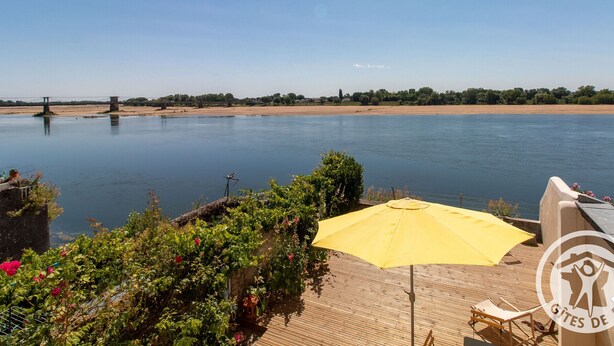 Uitzicht op de rivier met een houten terras, een gele parasol en een brug op de achtergrond.
