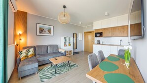 A modern living room with a grey sofa, a wooden coffee table, and a dining area with a wooden table and chairs. - Apartamenty Sun & Snow Nowe Hallerowo (Wladyslawowo)