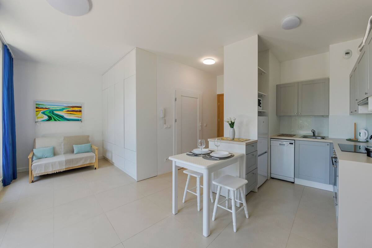 A compact kitchen with a dining area, white cabinetry, and a small table set for two.