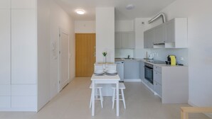 A compact kitchen with white cabinets, a dining table with two chairs, a small countertop, and a wooden door. - Apartamenty Sun & Snow Nowe Hallerowo (Wladyslawowo)