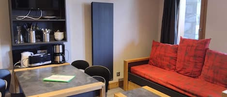 A compact living space with a dining table, chairs, a sofa, and a built-in bookshelf.